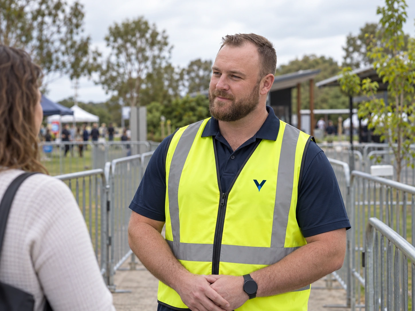 Event security officer speaking with a visitor beside an outdoor entry lane.